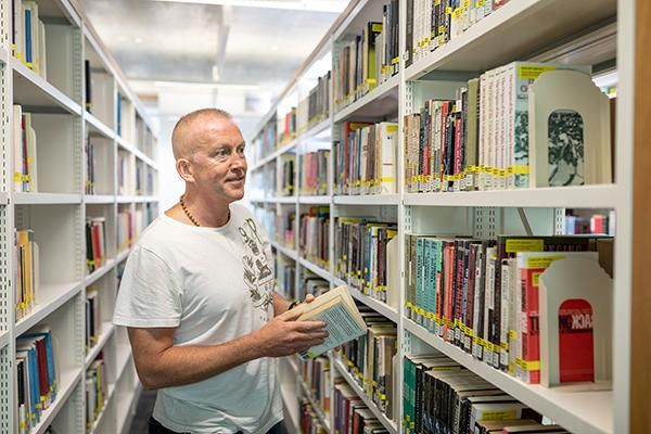 Student holding a book in between library shelves