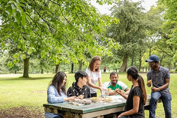 A group of students having a picnic on a picnic bench in Hyde Park