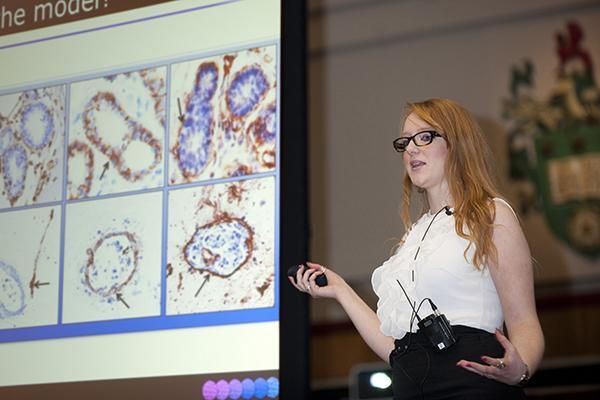 Student presenting at a conference standing in front of a screen with their research on