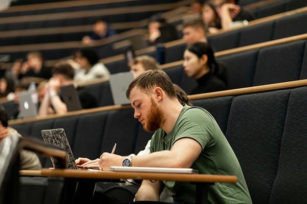 A student taking notes on paper in a lecture theatre
