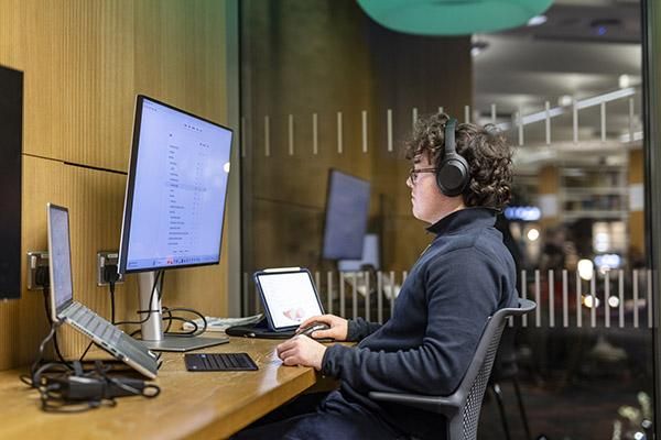 Student wearing headphones using a computer in a bookable study space