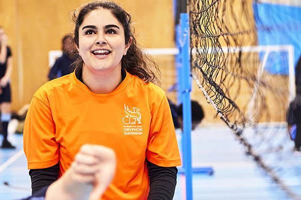 A student volunteer in an orange t-shirt teaching volleyball