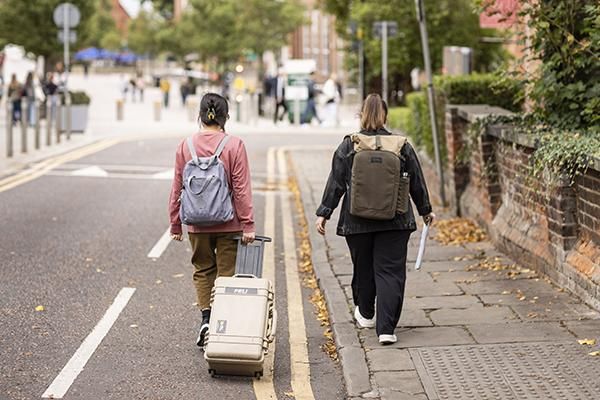 Two students walking on campus, one with a suitcase