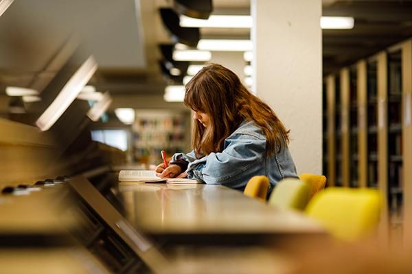 Student writing at a desk in a library
