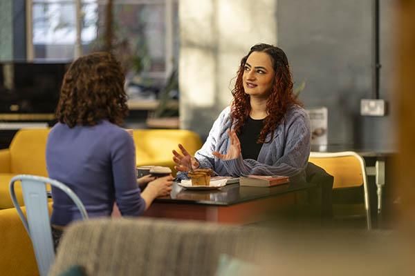 Two students sit chatting at a small table inside Common Ground cafe.