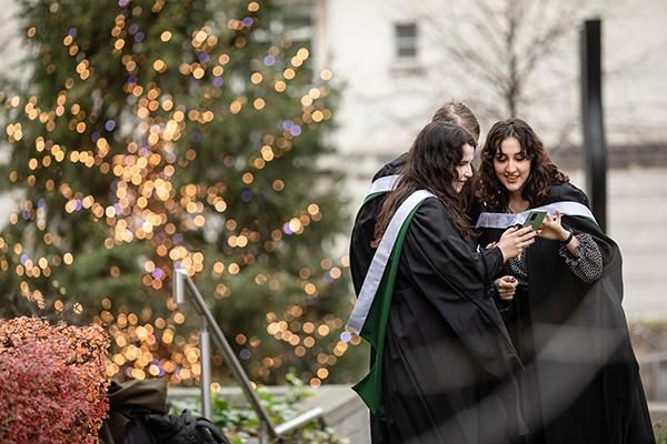 Three graduates looking at a photo on a phone by the Christmas tree on graduation day