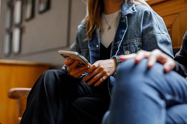 Close up of a student's denim jacket and their hands holding a phone