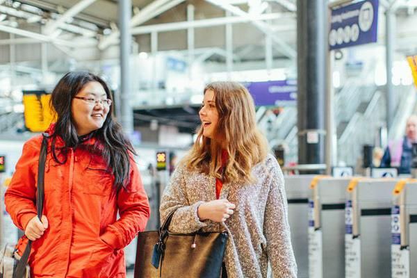 Two students in Leeds railway station near the barriers and departure boards