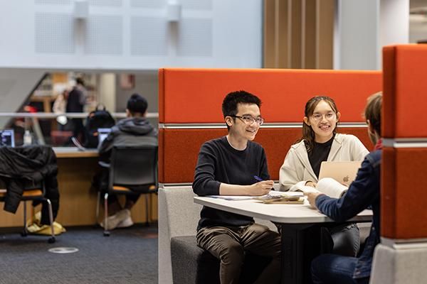 Two students chatting while working in a booth in the Laidlaw Library