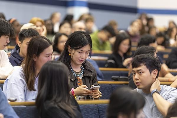 Students in a lecture theatre. One is using their phone.