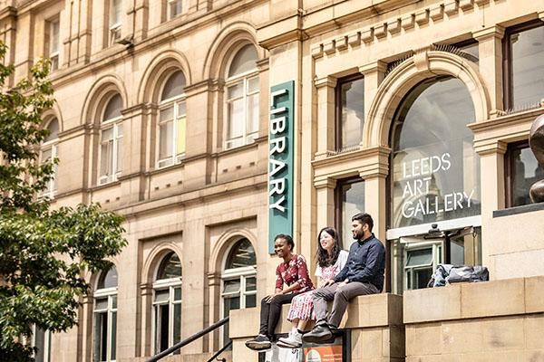 Three students sitting on a wall outside the entrance to Leeds Art Gallery