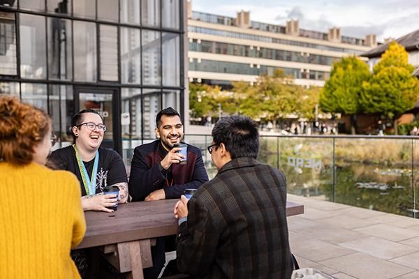 Students and a support worker drinking hot drinks on a bench by Roger Stevens pond