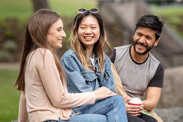 Three students sitting on a rock chatting on campus