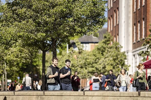 Two students walking on campus holding hot drinks and chatting