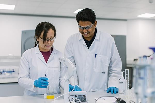 Two students wearing lab coats working together in a lab