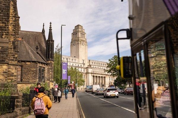 The Parkinson Building clock tower seen from Woodhouse Lane on a sunny day, with students walking along the pavement.