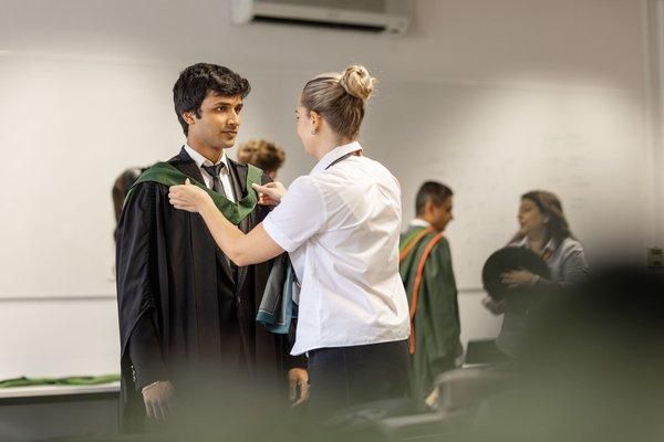 A member of staff adjusts a graduate’s green hood in the gowning room before the ceremony.