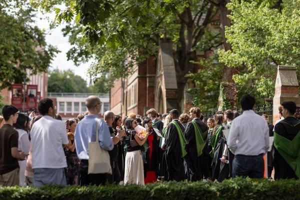 A crowd of graduates in gowns and their guests gather under the trees outside the Great Hall after the ceremony.