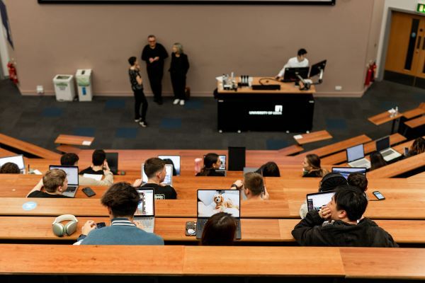 Looking down at a lecture hall. A number of students can be seen, each with their laptops open displaying their work.