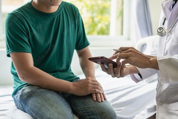 A person sat in a bright medical setting, chatting to a medical professional who is showing them something on a phone.