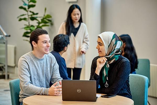Two students sitting at a table chatting with a laptop on the table