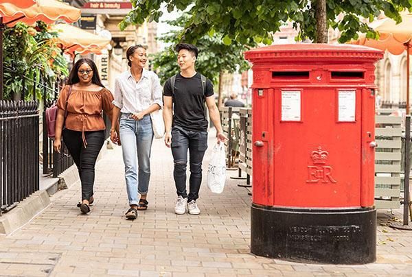 Three students carrying shopping bags next to a red post box in Leeds city centre