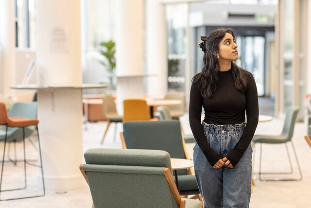 A student stands inside a large, communal space and looks upwards to their left.