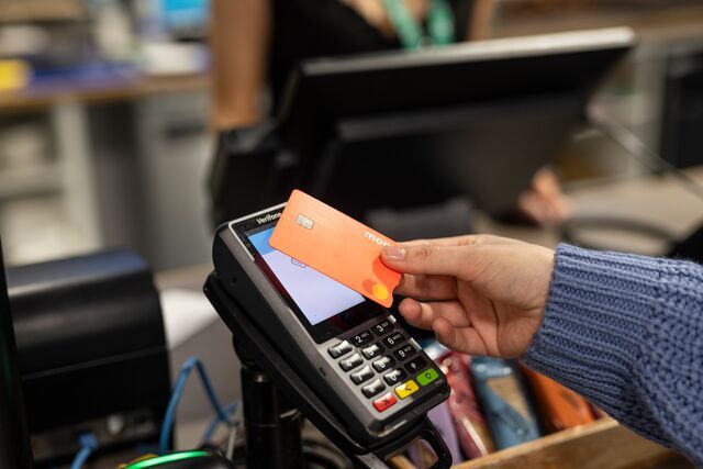A hand hovers a red, Monzo bank card over a card reader to pay.