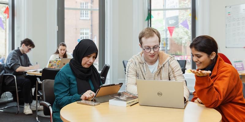 A group of mature students sitting at a table working on laptops and tablets