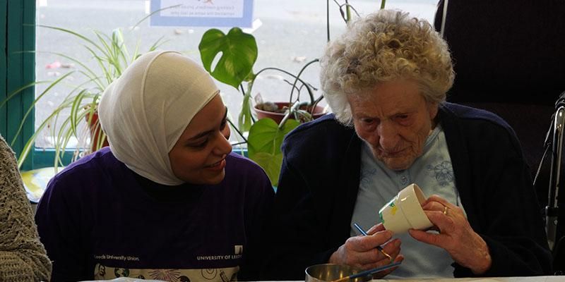 An intercultural ambassador painting a pot with an elderly person