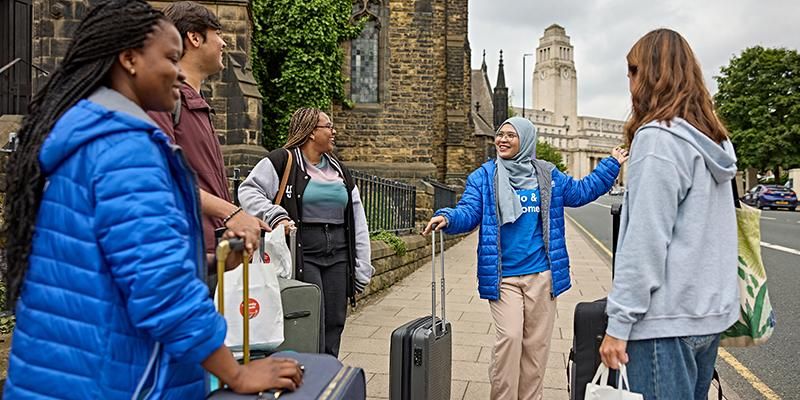 A Welcome team ambassador greeting students with suitcases in front of the Parkinson building