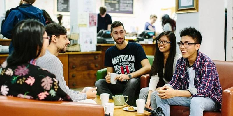 A group of students chatting together in a cafe with hot drinks and cake.