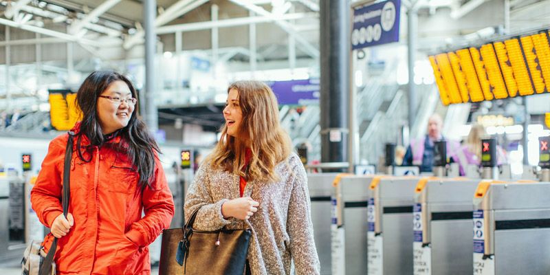 Two students in Leeds railway station near the barriers and departure boards