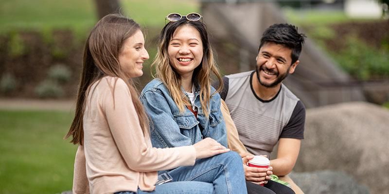 Three students sitting on a rock chatting on campus