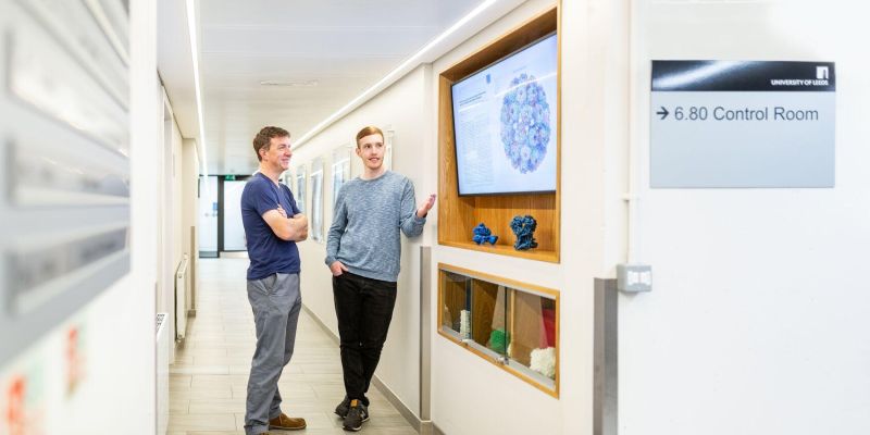 Postgraduate research student, discusses a research paper, which is displayed on a screen, with their tutor.