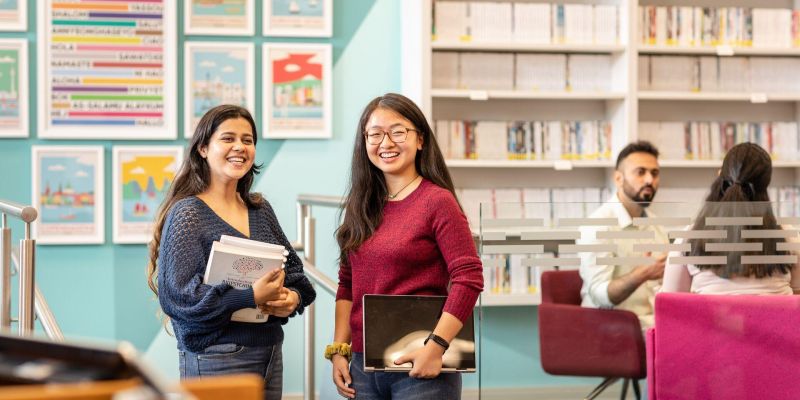 Two students holding books and smiling in the Language Zone.