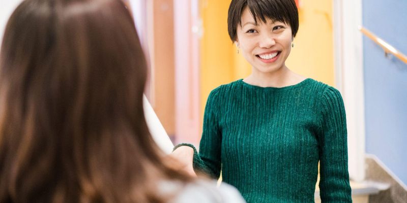 A person stands at the bottom of a stairway in Leeds University Union and smiles at someone who is facing them.