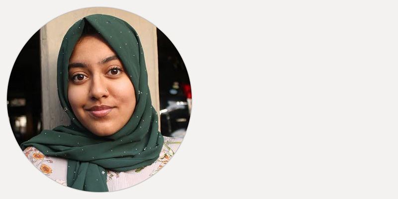 Zainab smiling, stood in front of a pillar on campus.