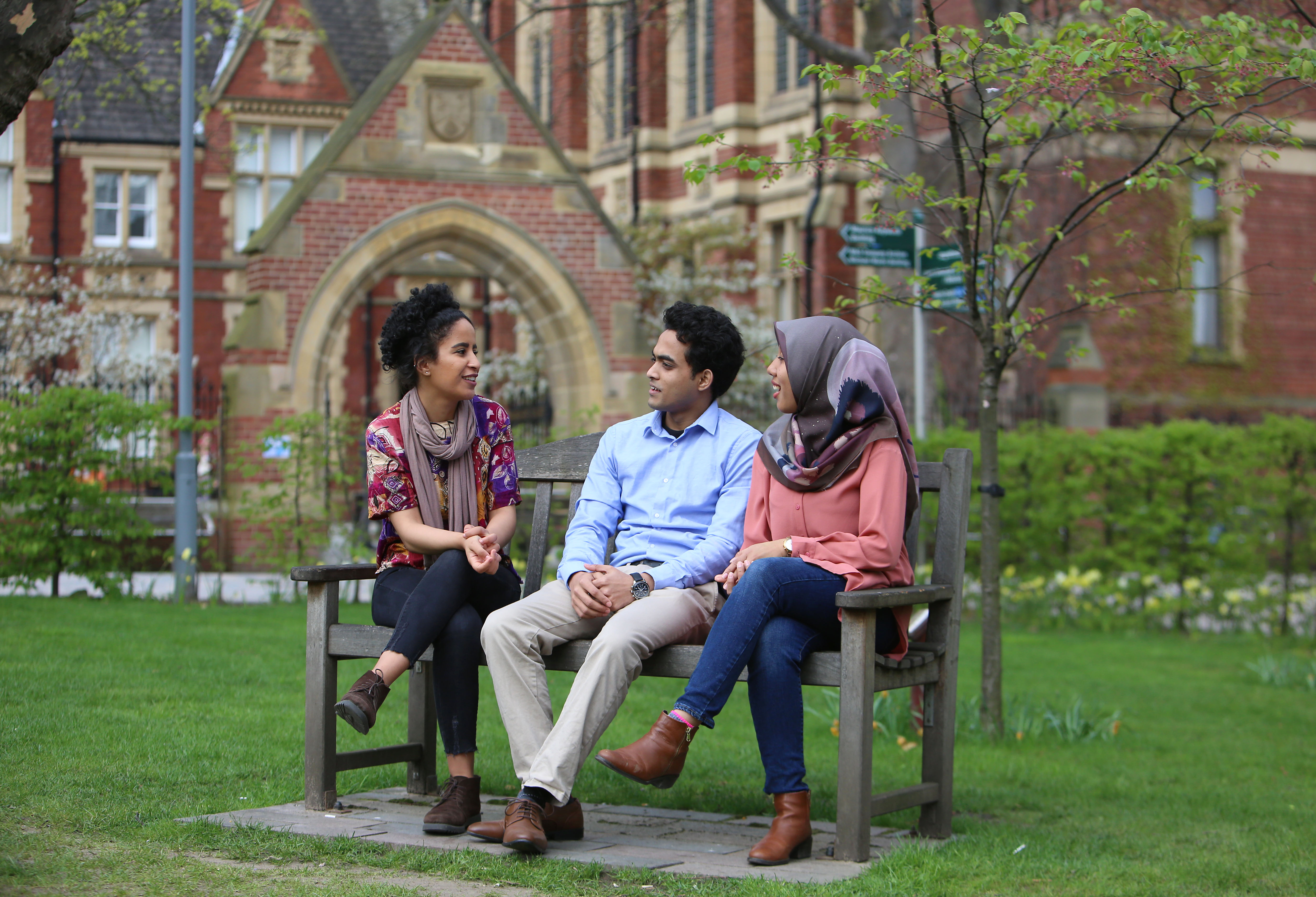 Three students sit on a bench talking.