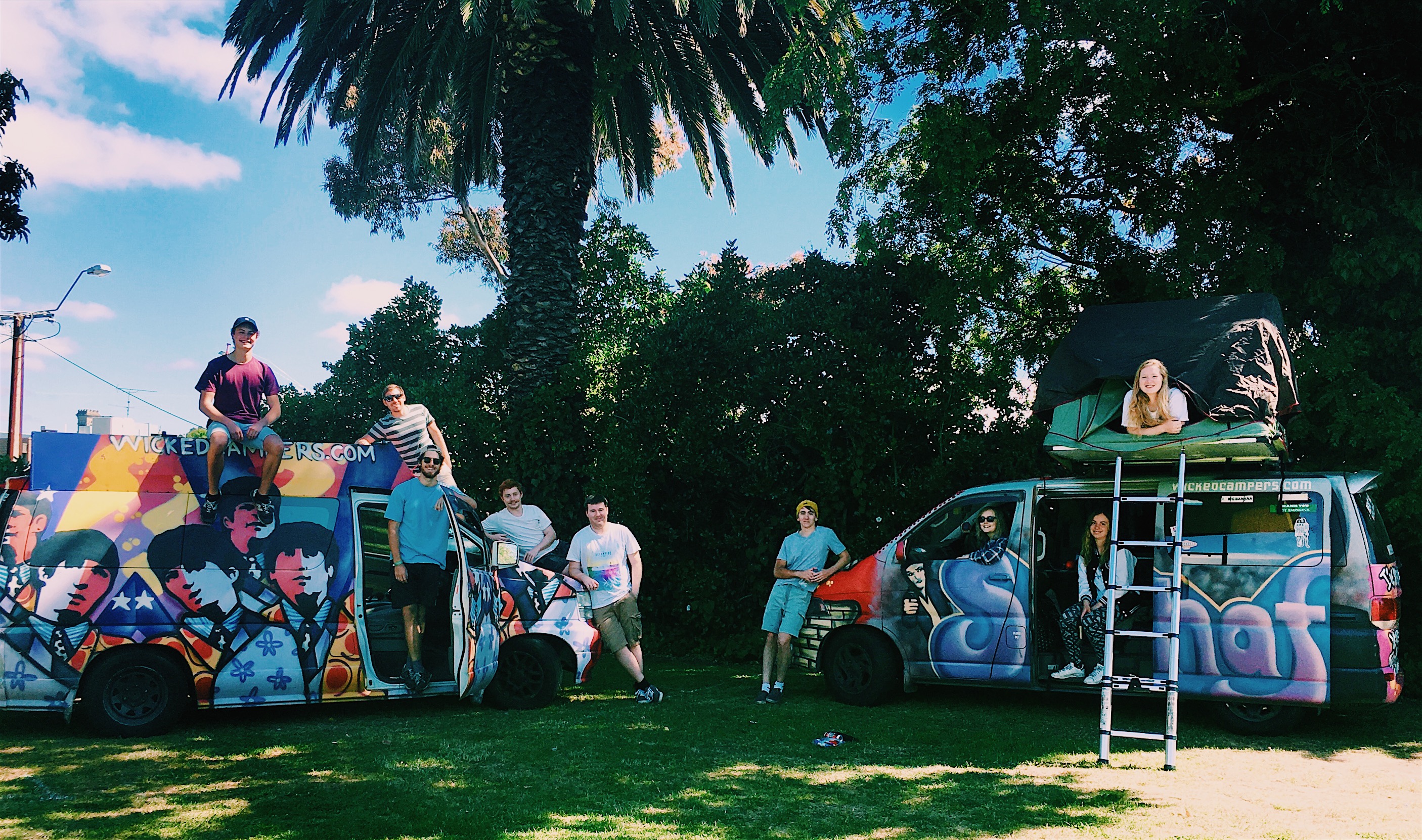 A group of people gathered around two brightly painted camper vans. 