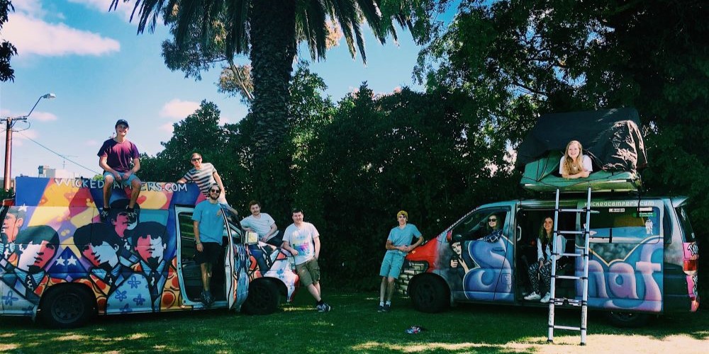 A group of people gathered around two brightly painted camper vans. 