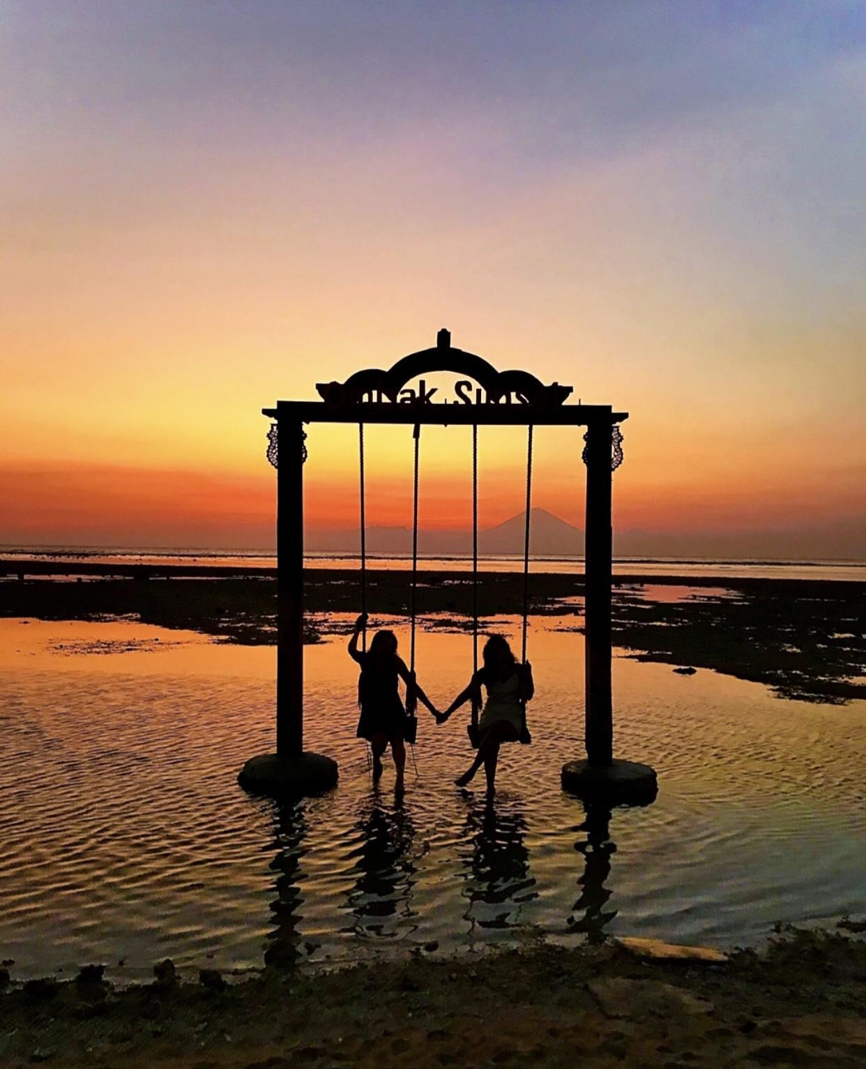 Two girls sitting on a swing in Indonesia at sunset