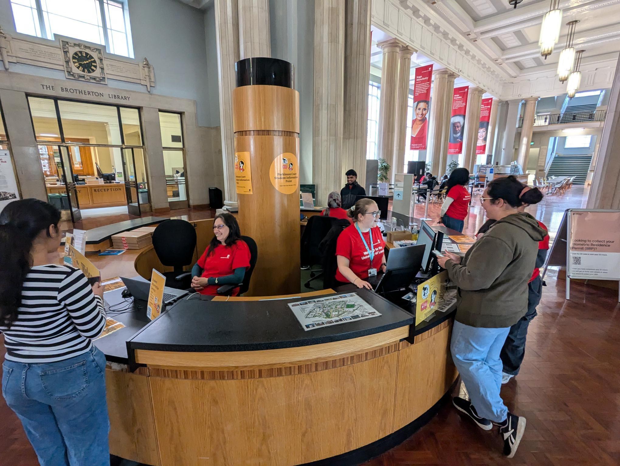 A group of students are standing at the welcome hub speaking with ambassadors