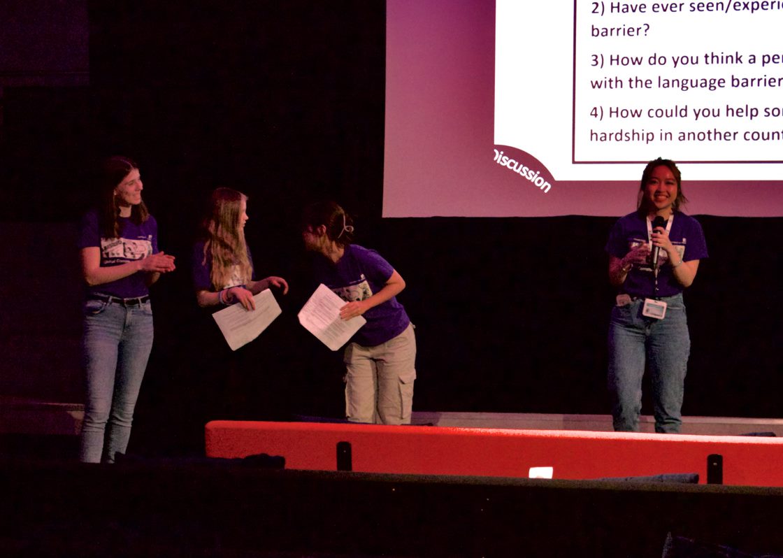 Four students in front of a screen leading a Q&A session and holding notes in their hands.